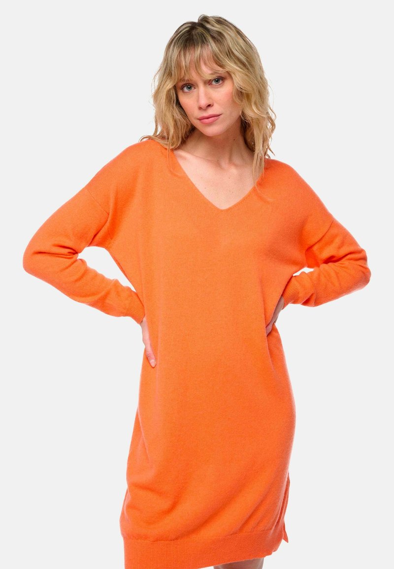 Robe en tricot orange à col en V, à manches longues, coupe décontractée et poignets côtelés. Sa texture douce et ses fentes latérales ajoutent un détail fonctionnel.
