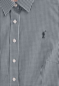 Schwarz-weiß kariertes Hemd mit Button-Down-Kragen, ausgestattet mit hellen Knöpfen und einem dezenten gestickten Logo auf der Brust.