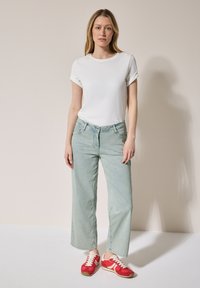 Vit bomull T-shirt med rullade ärmar, ljusblå vida jeans och röda sneakers med vita detaljer, stående mot en neutral bakgrund.