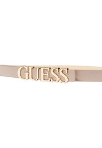 Cintura beige con materiale sintetico liscio e un prominente logo "GUESS" in tonalità oro sulla parte anteriore. Design semplice ed elegante.