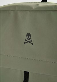 Tissu vert olive avec un crâne et des os croisés noirs imprimés au centre au-dessus d'une couture piquée et d'une sangle noire en dessous.