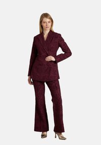 Traje burdeos con un blazer de doble botonadura y pantalones acampanados. La tela tiene un diseño texturizado y se complementa con tacones metálicos.