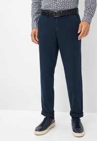 Pantaloni di cotone blu navy con vestibilità dritta, tasche frontali, orli con risvolto e una cintura in pelle nera. Abbinati a scarpe da ginnastica scure.