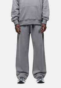 Grijze sweater en bijpassende broek van zacht materiaal, met een voorzak, een tailleband met trekkoord en subtiele logodetails op de broek.