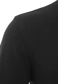 Dettaglio ravvicinato di un tessuto a maglia nera che mostra cuciture dettagliate lungo la cucitura della spalla di un indumento.
