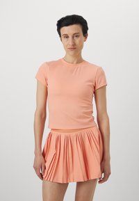 Conjunto deportivo de color melocotón que incluye una camiseta ajustada de manga corta con cuello redondo y una falda plisada con cintura elástica.