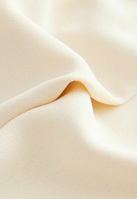 Svijetložuti materijal s mekanom, teksturiranom površinom, s nježnim nabora i drapiranjima. Materijal izgleda glatko i blago sjaji.