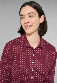 Camicia bordeaux con colletto, caratterizzata da un motivo a spirale bianco e chiusura a bottoni, realizzata in un tessuto morbido e testurizzato.