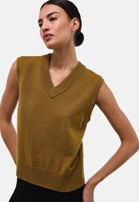 Un pull en tricot sans manches de couleur moutarde avec un col en V profond, un col et un ourlet côtelés, présentant une texture douce et une coupe décontractée.