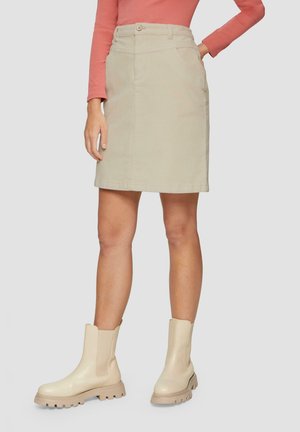 Beige denimrok met een frontale knoopsluiting, twee zijzakken en een rechte snit; gecombineerd met beige enkellaarsjes met een dikke zool.