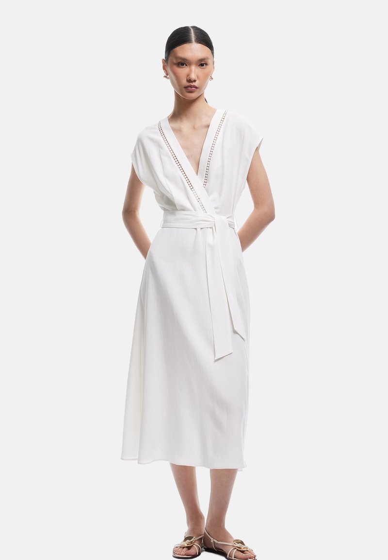 Weißes Wickelkleid mit kurzen Ärmeln, tiefem V-Ausschnitt, tailliertem Bund mit Knoten und dekorativer Naht entlang des Ausschnitts. Seidige Textur.