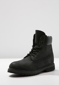 Bottine en cuir noir avec un bout arrondi, lacets à l'avant et col rembourré. Présente un panneau latéral texturé et une semelle en caoutchouc.
