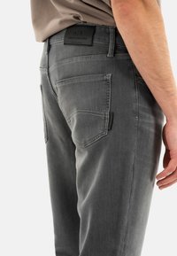 Jeans de mezclilla gris con corte recto, con bolsillos traseros y un parche de logotipo de la marca cosido en la cintura. Textura suave, diseño minimalista.