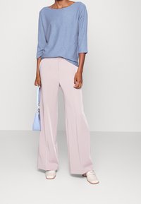 Ljusblå stickad topp med vid hals och trekvartsärmar, parat med blekrosa vida byxor. Ljusblå handväska, krämfärgade loafers.