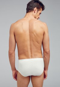 Culotte bianche a coste con una texture morbida, dotate di una vita elastica con marchio. La schiena del modello è mostrata, evidenziando la vestibilità e il design.