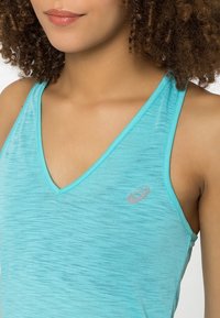 Débardeur de sport turquoise avec un col en V, fabriqué en tissu léger et texturé. Il présente un petit logo gris sur la poitrine.