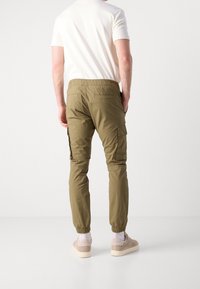 Kaki cargo-byxor med elastisk midja, sidofickor och nedtrappade benfållar. Bärs med en ljusfärgad t-shirt och sneakers.