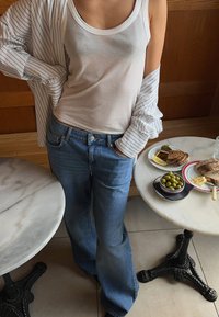 Vaaleansinisiä, leveälahkeisia farkkuja yhdistettynä valkoiseen toppiin, jonka päällä on rennosti laskeutuva raidallinen paita. Ruokaa ympärillä marmoripöydillä.