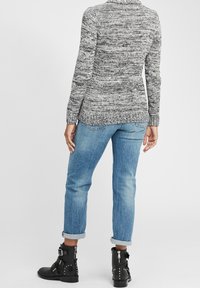 Pull tricot gris et noir à manches longues, assorti à un jean bleu clair à revers et des bottines noires à boucles et clous.