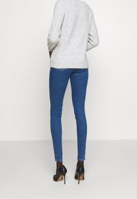 Vaaleanharmaa neulepaita, jossa on teksturoitu neulos, käytettynä sinisten slim-fit-farkkujen ja mustien korkokenkien kanssa, nähtynä takaa.