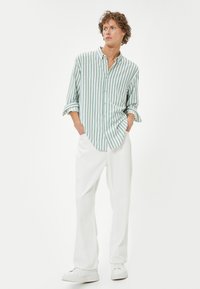 Camisa de botones a rayas en verde claro y blanco, combinada con pantalones sueltos blancos y zapatillas blancas. Ajuste casual y relajado con mangas arremangadas.