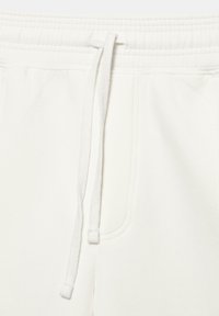 Pantalon de survêtement blanc avec taille élastique et cordons blancs, doté de poches latérales et de détails de coutures visibles.
