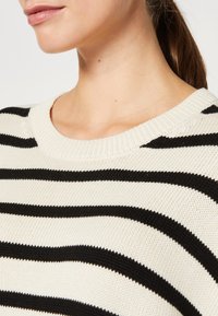 Gestreifter Strickpullover mit abwechselnd schwarz-weißen Streifen, rundem Ausschnitt und strukturiertem Stoff. Mit einer lässigen Passform gestaltet.