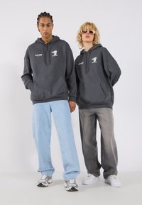 Mørkegrå hettegensere med framfester og hvite grafiske detaljer, kombinert med lyseblå og grå baggyjeans og sneakers.