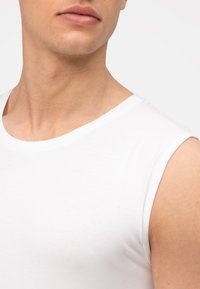 Witte mouwloze katoenen shirt met een ronde hals. Soepele textuur en aansluitend ontwerp, zichtbaar schouder- en halsgebied.