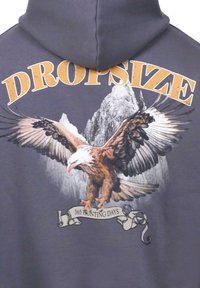 Sudadera con capucha gris que presenta un gran gráfico de un águila sobre el texto "DROPSIZE" y un banner que dice "365 DÍAS DE CAZA."
