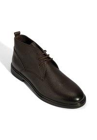 Bottes chevilles en cuir marron avec une finition texturée, avec un bout rond, un laçage à l'avant et une semelle en caoutchouc plate.