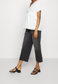 Hvid, kortærmet bluse med hulmønster, parret med højtsiddende, cropped sorte denimbukser og sorte sandaletter med stropper.