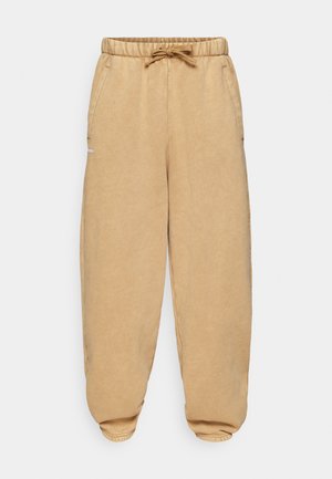 Béžové joggingové kalhoty vyrobené z měkké tkaniny, s elastickým pasem na šňůrku, bočními kapsami a zúženými manžetami.
