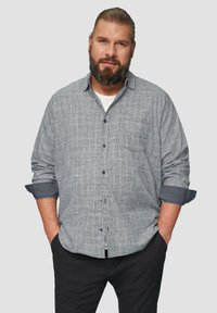 Grijs geruit overhemd met een borstzak, opgerolde mouwen en marineblauwe accenten. Gecombineerd met zwarte broek, weergegeven op een neutrale achtergrond.