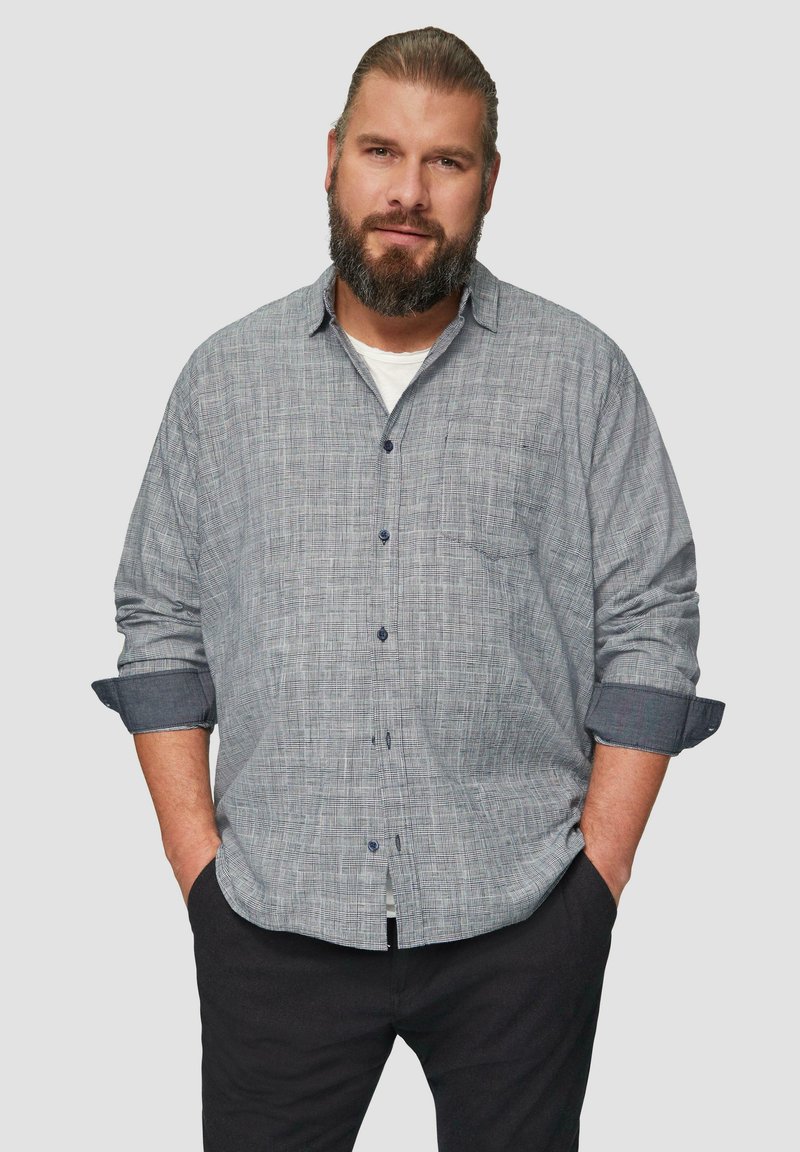 Grijs geruit overhemd met een borstzak, opgerolde mouwen en marineblauwe accenten. Gecombineerd met zwarte broek, weergegeven op een neutrale achtergrond.