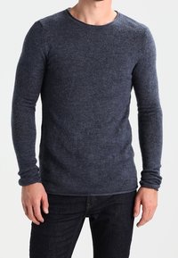 Navyblaues Strickoberteil mit langen Ärmeln aus weichem Stoff, mit rundem Ausschnitt und taillierter Silhouette, kombiniert mit dunklen Jeans.