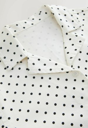 Fehér galléros ruhadarab fekete pöttyökkel, hajtott gallérral és látható gombbal az elülső nyílás közelében.