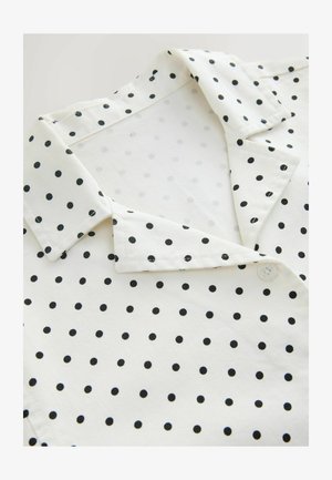 Fehér galléros ruhadarab fekete pöttyökkel, hajtott gallérral és látható gombbal az elülső nyílás közelében.