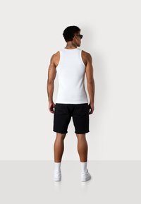 White ribbed tank top, black denim shorts with frayed hem, white sneakers, and white socks, viewed from the back on a plain background.