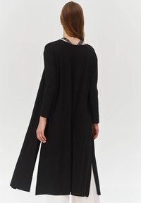 Czarna sukienka z długim rękawem i bocznymi rozcięciami, wykonana z gładkiego materiału. Ma luźny krój i okrągły dekolt. Prosty design, bez wzorów.