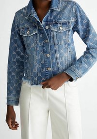 Jeansjacka i ljusblå färg med subtilt logomönster, klassisk krage, bröstfickor, knappstängning och fransad fåll.