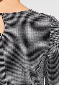 Rückseite eines schwarz-weißen Hahnentrittmusters mit einem Schlüssellochausschnitt, der am Nacken mit einem kleinen Knopf geschlossen wird.