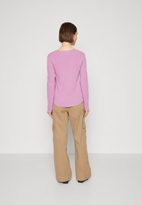 Pitkähiha pieni paita, jossa on pyöreä kaula-aukko, yhdistettynä beigeihin cargo-housuihin, joissa on sivutaskut, seisoo neutraalin taustan edessä.