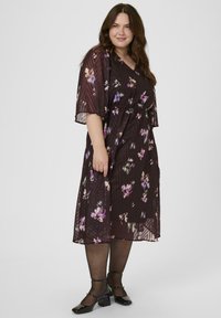 Sötét virágmintás ruha rövid ujjakkal, V-nyakkivágással és elasztikus derékrésszel. Átlátszó réteg borítja, lila és fehér virágmintákkal díszítve.