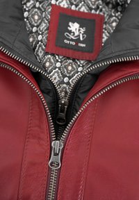 Rote Lederjacke mit einem schwarzen Reißverschluss auf der Vorderseite, ausgestattet mit einem gemusterten Innenfutter und einem "OTTO KERN"-Etikett. Sichtbare Reißverschlussdetails.