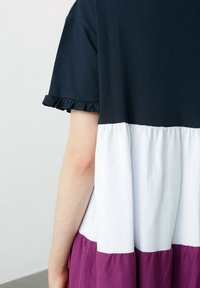 Haut bleu marine avec manches volantées, section centrale blanche et bas couleur prune. Matière coton doux, taille cintrée pour une silhouette ajustée.