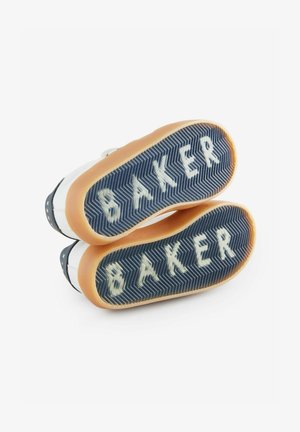 Zapatillas blancas con suelas de goma azules, que presentan un patrón de espiga y el texto "BAKER" en blanco. Bisel de goma marrón en las suelas.