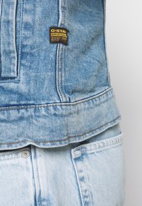 Ljusblå denimjacka med en G-Star Raw-lapp, med synlig sömnad och en lätt fransad fåll, i kombination med ljusblå jeans.