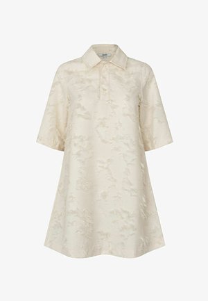 Túnica tipo polo de manga corta en color crema claro con un patrón texturizado, que presenta un cuello clásico y una silueta amplia tipo línea A.