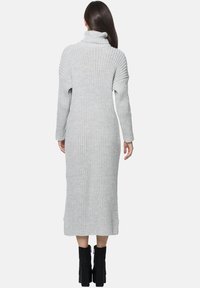 Hellgraues, geripptes Strickkleid mit Rollkragen und langen Ärmeln, das bis zur Mitte der Wade reicht, kombiniert mit schwarzen Stiefeln mit Absatz. Vertikale Strukturdetails sind sichtbar.